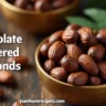 Chocolate covered almonds in a bowl, topped with fresh greenery