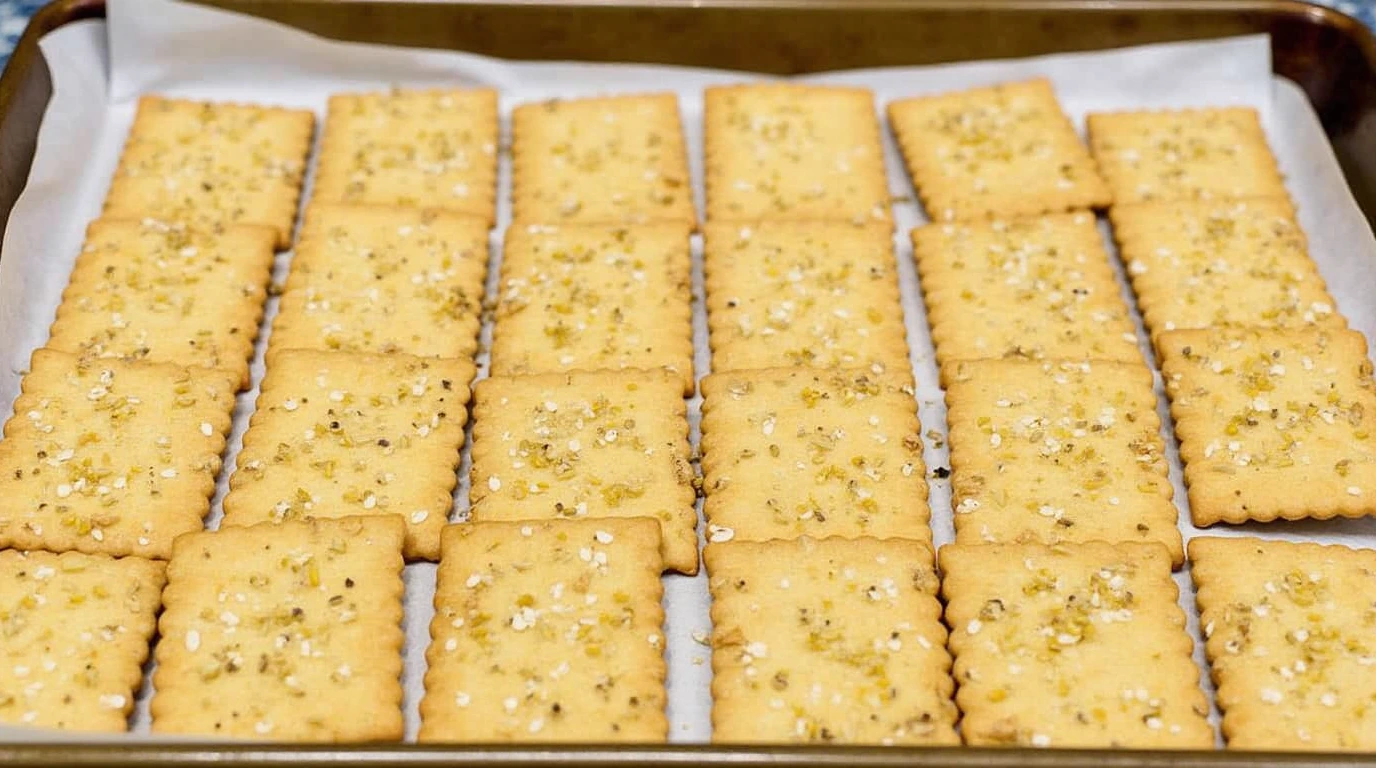 Unbaked gluten free crackers topped with sesame seeds on a tray.